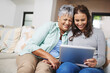© peopleimages.com - Help, tablet and woman teaching senior mother networking on internet, mobile app or website on sofa. Happy, bonding and elderly mom learning digital technology with female person in living room.