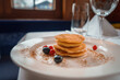 Close up view of luxuriously presented pancakes in Zermatt, Swiss ski resort. Neatly stacked on white plate with berries. Elegant dining setting in natural light.