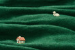 Miniature Homestead on Woolen Pasture. Tiny sheep and house figurines on a green wool fabric depicting a pastoral scene.