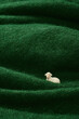 Tiny Sheep on Green Woolen Hills. A miniature sheep figurine placed on green wool fabric, mimicking rolling hills.