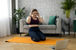 © mdyn - Sporty plus size woman in sportswear working out at home. Sports, activity and weight loss concept. Young happy woman in leggings exercising on the mat, watching online video via laptop
