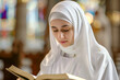 Portrait of Caucasian nun in white habit reading bible book in the church