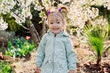 Smiling cute child girl in jacket in blooming garden.