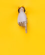 A wooden hand protrudes from a torn hole in yellow paper and points its index finger downwards. Concept of direction, adjustment and assistance. Mannequin, robot.