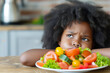 Displeased African American boy rejects salad, unhappy with meal