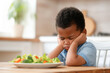 Unhappy afro kid rejects salad, displeased by healthy meal