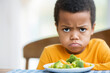 Unhappy black boy rejects healthy salad, displeased expression