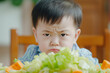 Little asian boy's aversion to salad evident in his unhappy expression