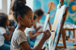 © Aaron Weiss - Cute African girl girl draws on an easel during a lesson in an art studio. The kid holds a brush in his hand and paints with paints. Child development
