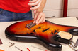 Guitar technician screws tremolo into the body of guitar.