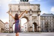 A happy tourist woman stands in front of the famous Victory Gate in Munich, Germany, during a city sightseeing trip