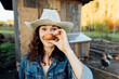 Funny Woman Farmer in denim with a fresh egg, making a funny face Cheerful Curly-haired woman showcases an egg at her countryside dwelling