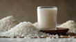 Glass of milk with piles of uncooked rice and a wooden spoon on a neutral background.