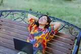 Fototapeta Zwierzęta - Asian freelancer with laptop enjoying relaxing on bench in park in summer Freelance lifestyle portrayed by a woman engaging with technology in a peaceful park setting