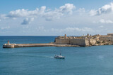Fototapeta Uliczki - A boat enters Valletta Bay passing near the Ricasoli East Breakwater, Kalkara, Malta