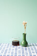 Glass cup of coffee with vase of dry flower on blue tile desk. mint wall background
