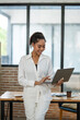 © Wasana - A delighted professional young woman reacts positively to content on her laptop at a wooden desk in a well-lit office space.