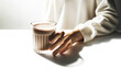 A person's hand gently cradling a ribbed glass filled with rich chocolate milk or cocoa against a white background with copy space. Concept healthy food and snacks, casual break, alternatives drinks