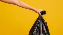 Hand Holding Garbage Bag Over Yellow Background