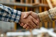 Closeup of a firm handshake between an architect and a client, construction site and blueprints in soft focus background
