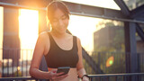 Fototapeta Mapy - Fitness happy asian woman using smartphone and resting after running on city in the morning, sunset