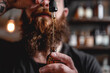 A man with a beard is holding a bottle of oil and pouring it into his mouth. Concept of relaxation and indulgence, as the man is taking a moment to enjoy the scent and taste of the oil