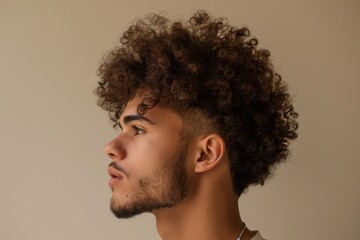 Wall Mural - Profile view of a young man displaying a stylish curly undercut hairstyle on a neutral background