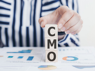 Wall Mural - The word CMO on a wooden blocks with womans hands. Business concept. CMO - short for chief marketing officer