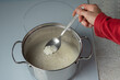 A spoon with rice in a woman's hand over a pot of boiling rice. Selective focus.