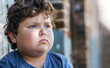 Little overweight boy sits on street alone. Looks sadly to side.Concept: children's complexes with excess weight, difficulties in communicating with peers.Closeup.Generative AI