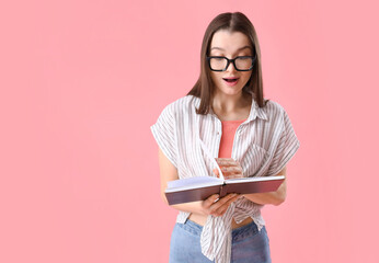 Sticker - Surprised young woman in eyeglasses reading book on pink background