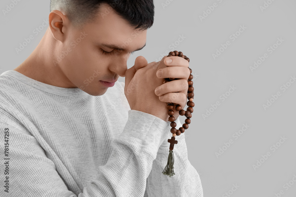 Young man with rosary beads praying on grey background
