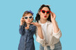 © Pixel-Shot - Beautiful pin-up woman and her daughter in sunglasses blowing kiss on blue background