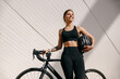 Smiling woman is standing with bike and protective helmet before cycling in city and looks away