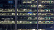 Office building exterior during late evening with interior lights on and people working inside night timelapse