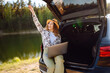 © maxbelchenko - Young woman sits in the trunk of a car and works on a laptop during her journey through the highlands. Work and travel.