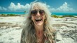 Portrait of a laughing woman with long white hair wearing sunglasses and a floral shirt standing on a beach