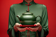 Woman in green Chinese clothing holding a green teapot against a red backgroun