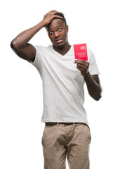 Canvas Print - Young african american man holding passport of Switzerland stressed with hand on head, shocked with shame and surprise face, angry and frustrated. Fear and upset for mistake.