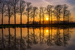 Bäume spiegeln sich im Wasser, im Hintergrund ein Sonnenuntergang