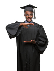 Poster - Young graduated african american man over isolated background gesturing with hands showing big and large size sign, measure symbol. Smiling looking at the camera. Measuring concept.