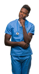 Wall Mural - Young african american doctor man over isolated background wearing surgeon uniform with hand on chin thinking about question, pensive expression. Smiling with thoughtful face. Doubt concept.