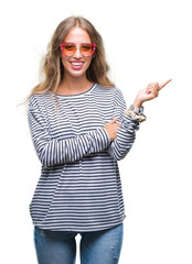 Sticker - Beautiful young blonde woman wearing sunglasses over isolated background with a big smile on face, pointing with hand and finger to the side looking at the camera.