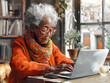 Elderly dark-skinned woman sitting at a table with a laptop in a casual cafe, leisurely browsing online.