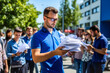 © Garnar - Man in blue shirt volunteering for a public referendum, actively engaging community in corporate sustainability campaign outdoors. Concept of company involvement in ecology initiatives
