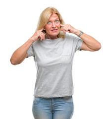 Wall Mural - Middle age blonde woman over isolated background covering ears with fingers with annoyed expression for the noise of loud music. Deaf concept.