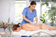 Professional young female massage therapist doing relaxing back massage to woman in cozy room of spa salon..