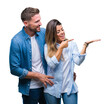 Young couple in love over isolated background amazed and smiling to the camera while presenting with hand and pointing with finger.
