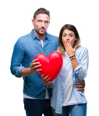 Wall Mural - Young couple in love holding red heart over isolated background cover mouth with hand shocked with shame for mistake, expression of fear, scared in silence, secret concept