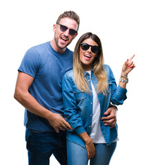 Wall Mural - Young couple in love wearing sunglasses over isolated background with a big smile on face, pointing with hand and finger to the side looking at the camera.